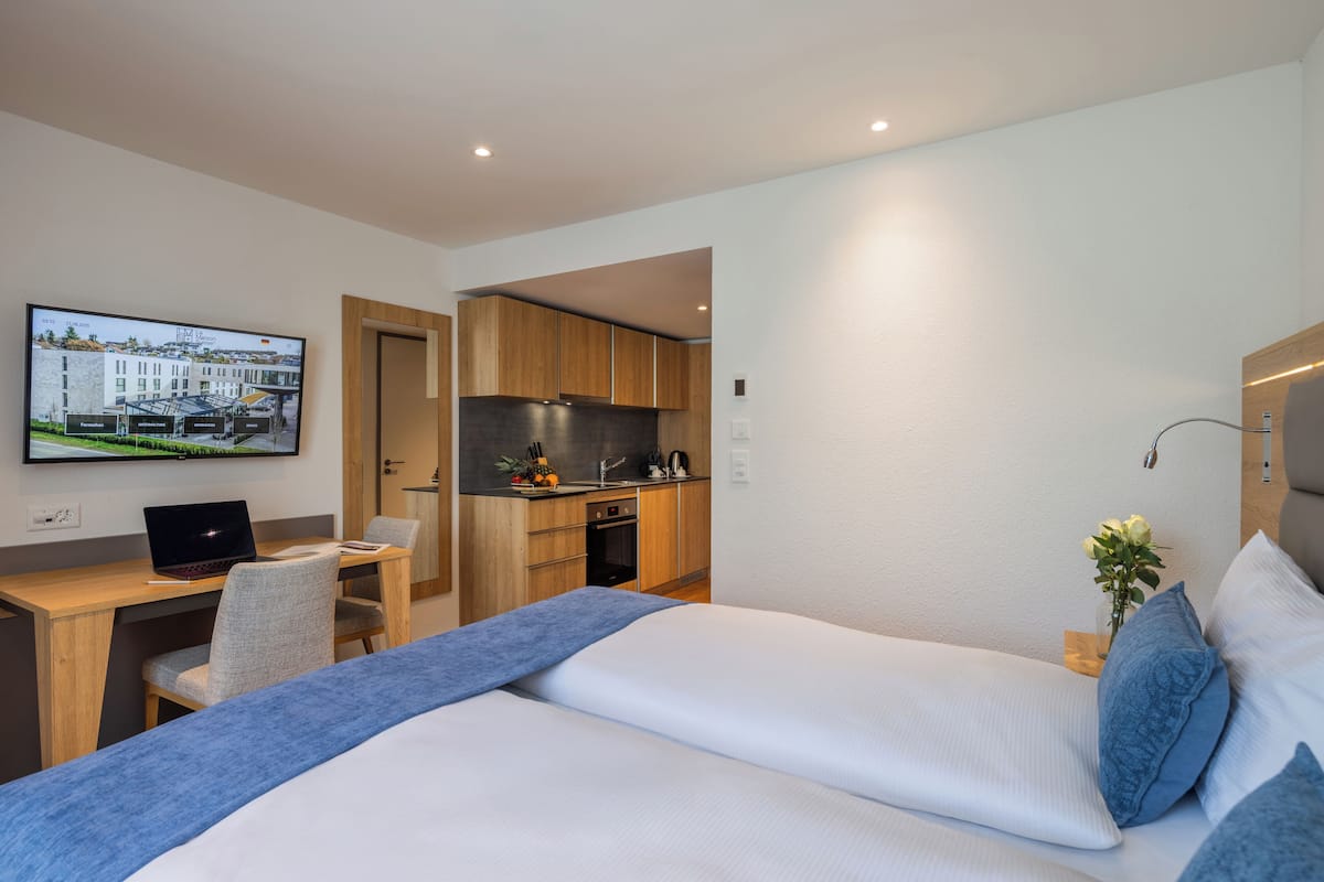 Een moderne hotelkamer met een bed, een bureau, een laptop, een televisie en een kitchenette.