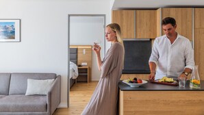 Una cocina moderna con armarios de madera, una zona de comedor con sofá gris y un vano que da a otra habitación.