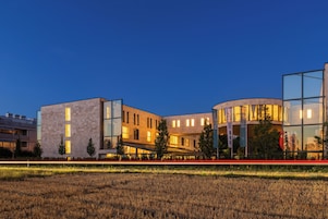 A modern building complex with multiple structures, including a curved glass facade and a rectangular building with a flat roof.