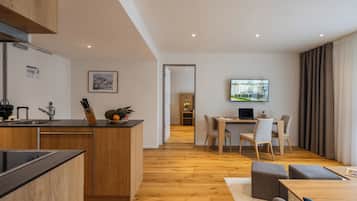 A modern kitchen with wooden cabinets and a central island, a dining area with a table and chairs, and a living space with a TV and seating.