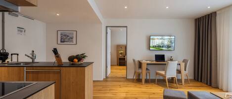 A modern kitchen with wooden cabinets and a central island, a dining area with a table and chairs, and a living space with a TV and seating.