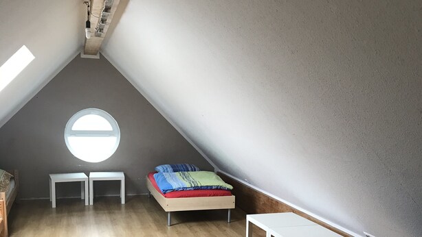 A small, sloped-roofed room with a bed, a table, and a bench. - Pension Yildirim - quiet and central vacation apartment (1) (Leverkusen)