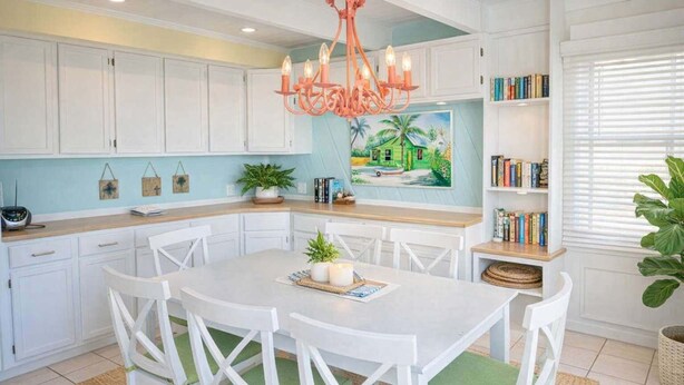 A kitchen with white cabinets, a round dining table with white chairs, a chandelier, and a bookshelf with books. - Caribbean Vibes House 3 Bedroom Home by RedAwning (South Padre Island)