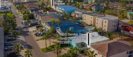 An aerial view of a coastal town with a prominent building at 126 E Carolyn Dr., South Padre Island, TX 78597. Nearby, Island Market is 3 miles away, and Kelly's Irish Pub is 7 miles away, both accessible by a 5-minute walk.
