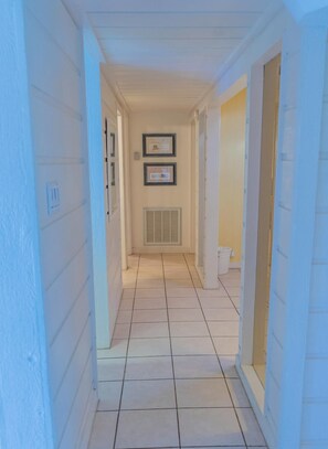 A narrow hallway with white walls and a tiled floor, leading to a door at the end. - Caribbean Vibes House 3 Bedroom Home by RedAwning (South Padre Island)