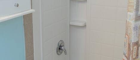 Een badkamer met hoekopstelling, voorzien van een badkuip, douche en toilet. Er is een handdoekrek en een plank boven de badkuip.