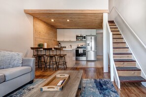 A modern living room with a sofa, a coffee table, and a kitchen area with a refrigerator, oven, and microwave.