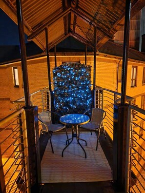 A covered outdoor seating area with a table and chairs, a decorative wall with lights, and a brick building in the background. - Bright Central Flat with Balcony and Free Parking! (Glasgow City)