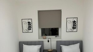 Ein Schlafzimmer mit zwei Einzelbetten, einem Nachttisch dazwischen, einem Fenster mit Jalousie und zwei Wandbildern.