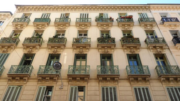 Ein mehrstöckiges Gebäude mit aufwendigen Balkonen, grünen Fensterläden und dekorativen Gesimsen.