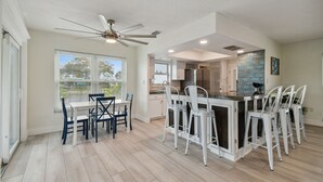 Une cuisine moderne avec des meubles blancs, un îlot central doté de tabourets et un ventilateur de plafond.