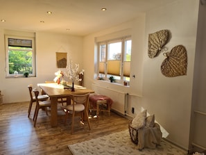 Enjoy meals in this dining area with a wooden table and chairs, surrounded by large windows and a cozy rug.