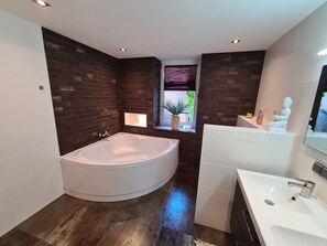 Relax in a spacious bathroom with a large bathtub, sleek sink, and a window offering a view of lush greenery.