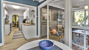 A modern kitchen with white cabinets, a dining area with a table and chairs, and a view through a glass door to an outdoor patio.