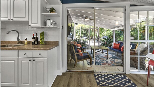A kitchen with white cabinets, a sink, and a countertop with bottles and a fruit bowl.