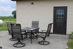 An outdoor patio with a table and four chairs, a door, and a view of a green field. - Prairieview Cottage Retreat - Hot Tub Sunsets (Sullivan)