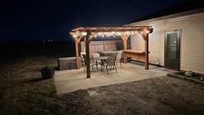 A covered patio area with a table and chairs, a wooden bench, and a pergola with string lights.