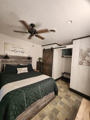 A bedroom with a bed, a ceiling fan, a wall-mounted TV, and a sliding barn-style door. - Prairieview Cottage Retreat - Hot Tub Sunsets (Sullivan)