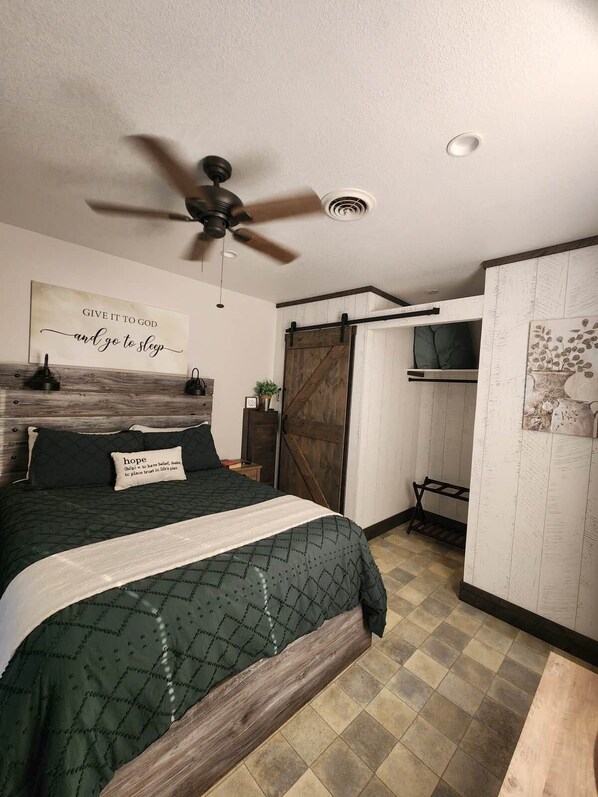 A bedroom with a bed, a ceiling fan, a wall-mounted TV, and a sliding barn-style door.
