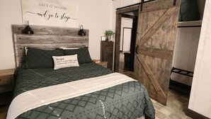 Une chambre à coucher avec un lit, un ventilateur de plafond, une tête de lit en bois, une porte coulissante de style grange et une citation inspirante sur le mur.
