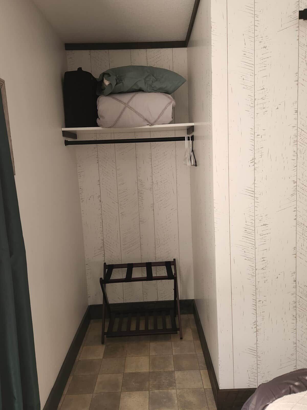 A small room with a bunk bed, a bench, and a shelf with pillows.