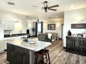 A modern kitchen with a central island, dark cabinetry, and a ceiling fan. - Prairieview Cottage Retreat - Hot Tub Sunsets (Sullivan)