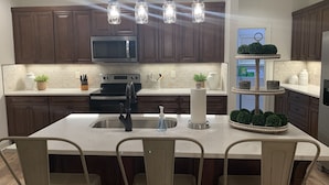 Una cocina moderna con armarios de madera oscura, un microondas de acero inoxidable, un horno negro y una isla blanca con taburetes de bar.