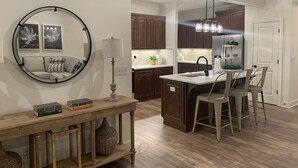 Una cocina moderna con armarios de madera oscura, una isla central con taburetes de bar, un espejo redondo y una lámpara colgante.