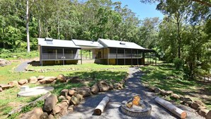A modern cabin with a covered patio and a fire pit area, surrounded by a natural forest setting. - Rainforest River Studio Kangaroo Valley (Upper Kangaroo River)