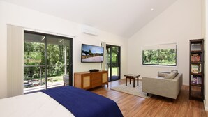 A modern bedroom with a large bed, a TV, and a sofa. - Rainforest River Studio Kangaroo Valley (Upper Kangaroo River)
