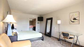 Een hotelkamer met een bed, een bureau met lamp, een stoel, een televisie en een spiegel.