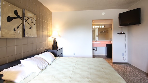 Een hotelkamer met een bed, een nachtkastje met een lamp, een aan de muur bevestigde televisie, en een badkamer zichtbaar door een geopende deur.
