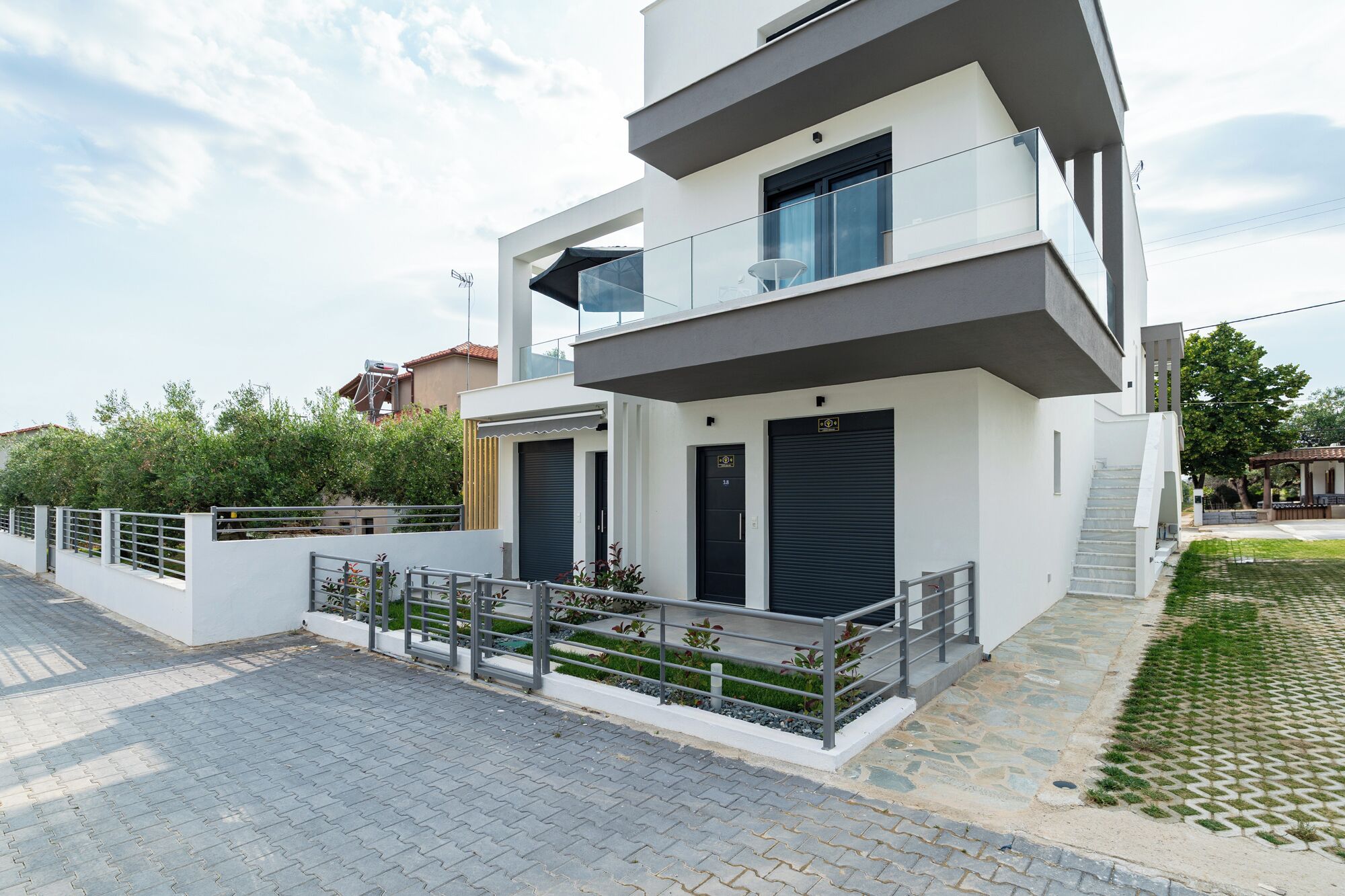 A modern two-story residential building with a flat roof, large windows, and a balcony.