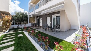 Un bâtiment moderne à deux étages doté d’un patio comprenant un espace extérieur aménagé avec des sièges et un jardin bien entretenu.