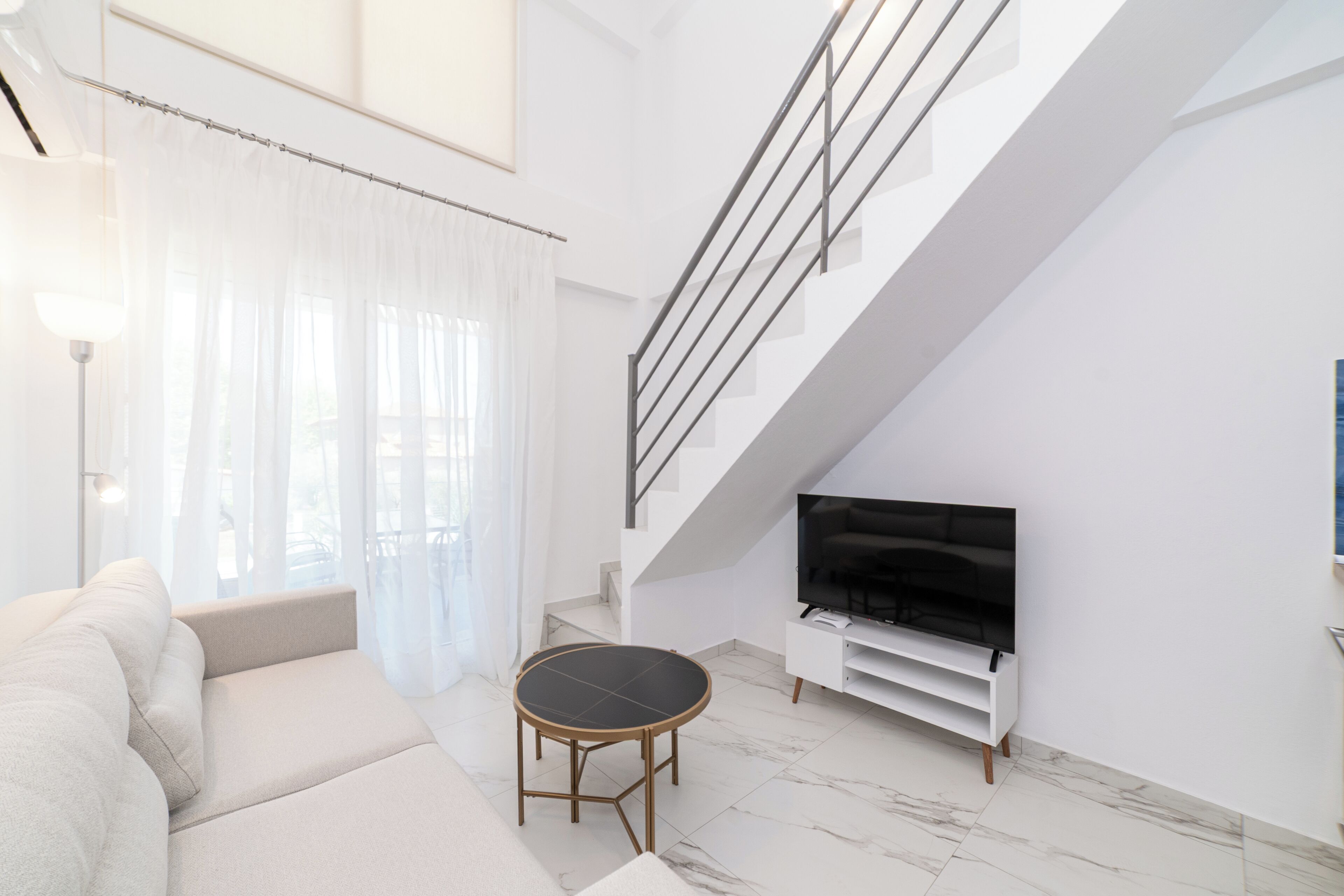 A modern living room with a sofa, a round table, a TV, and a staircase.