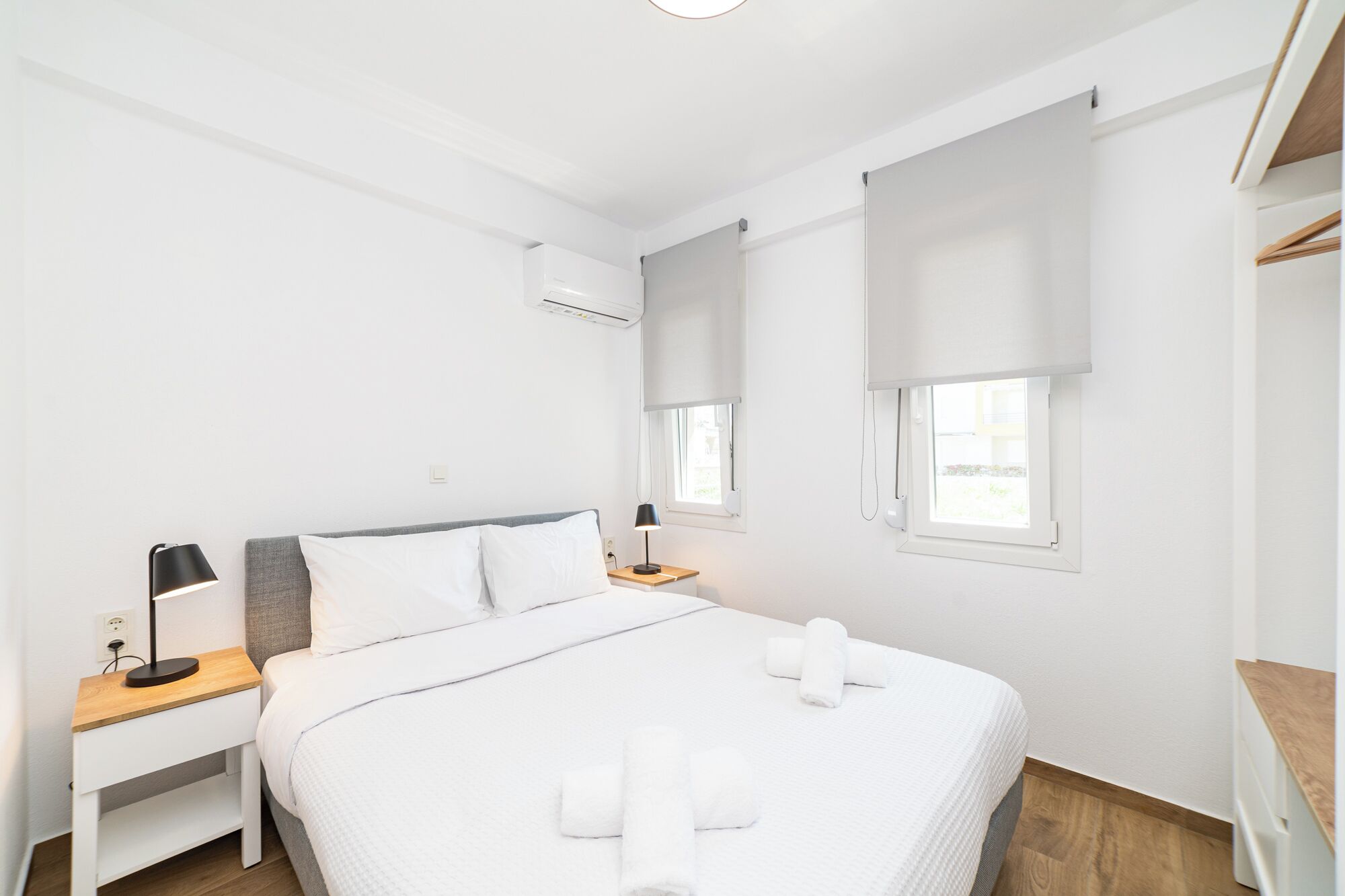 Habitación de hotel minimalista con cama, mesitas de noche, escritorio y ventana con persianas.