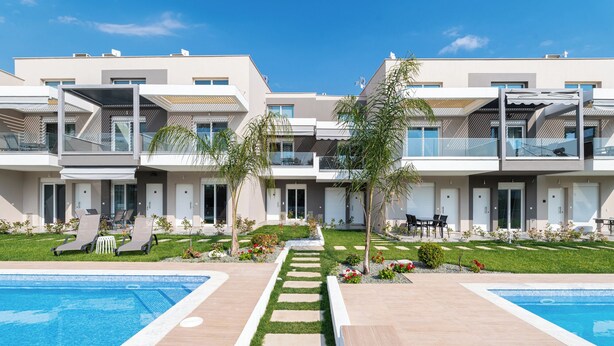 Un immeuble résidentiel moderne à plusieurs étages, doté d’une piscine, d’un espace extérieur aménagé et de jardins bien entretenus.