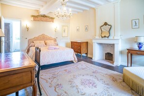 Ein Schlafzimmer mit einem großen Bett, einem hölzernen Schmuckkästchen, einem Kronleuchter, einem Kamin und einem großen floralen Teppich.