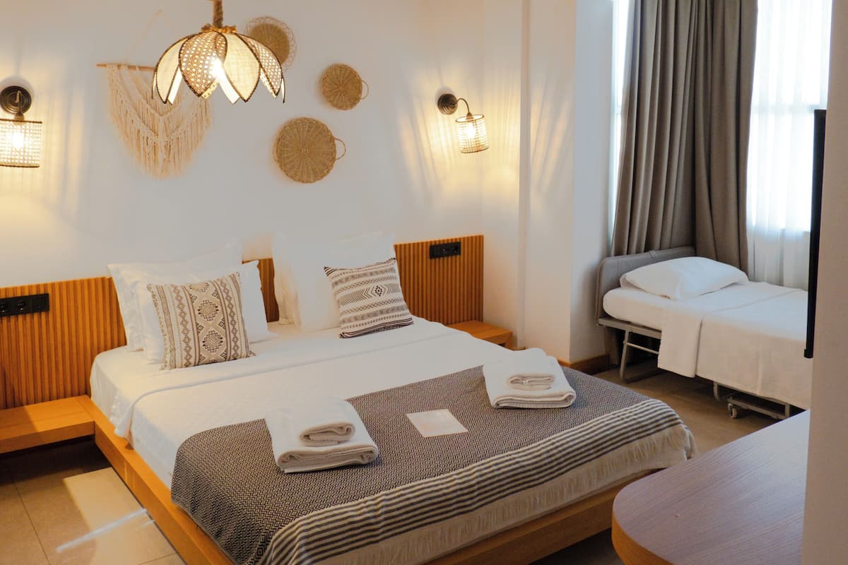 A bedroom with a large bed, a smaller bed, a table, and a ceiling with exposed beams.