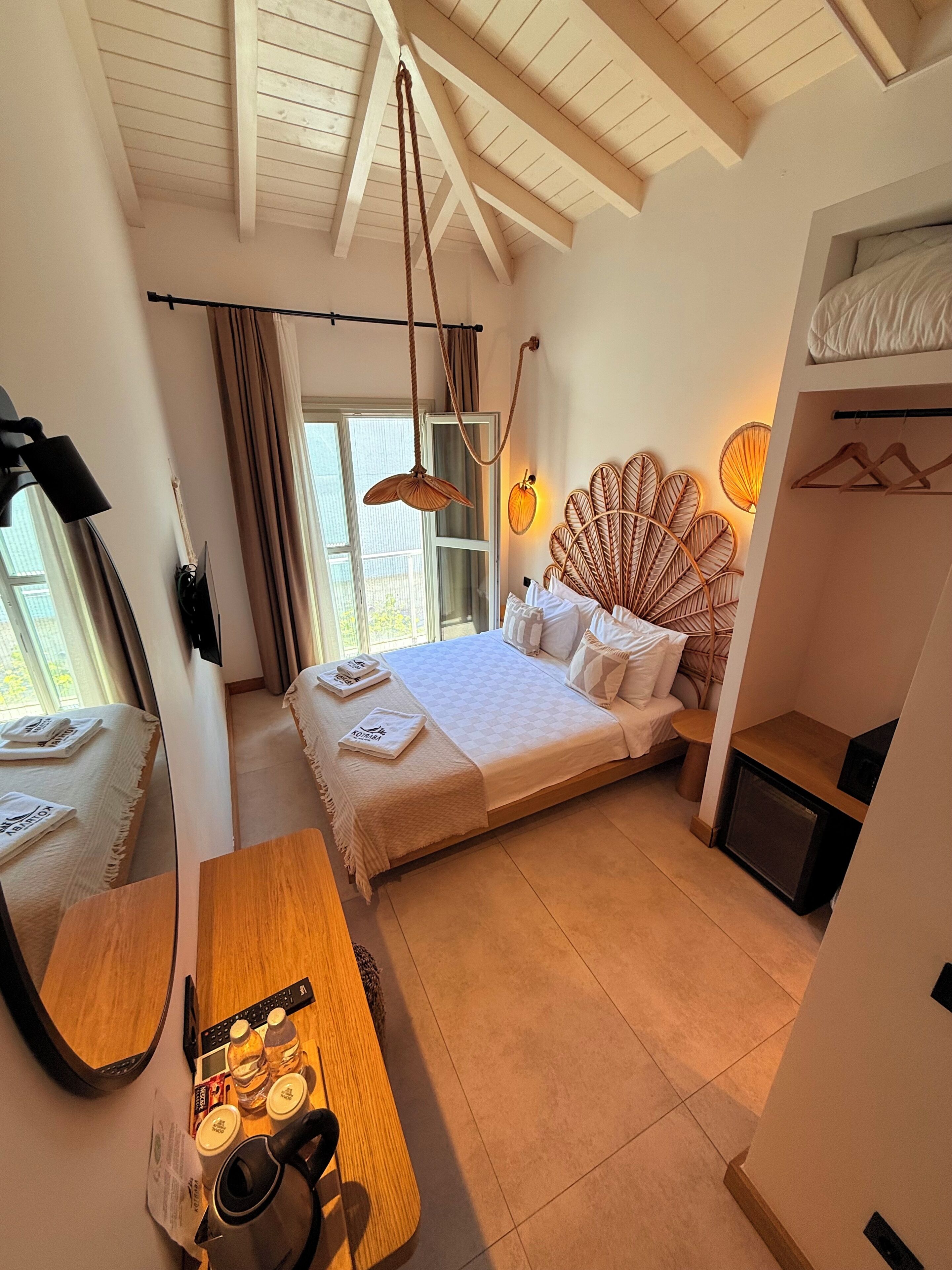Ein Schlafzimmer mit Bett, Nachttisch, Spiegel, Pendelleuchte und Blick ins Freie.