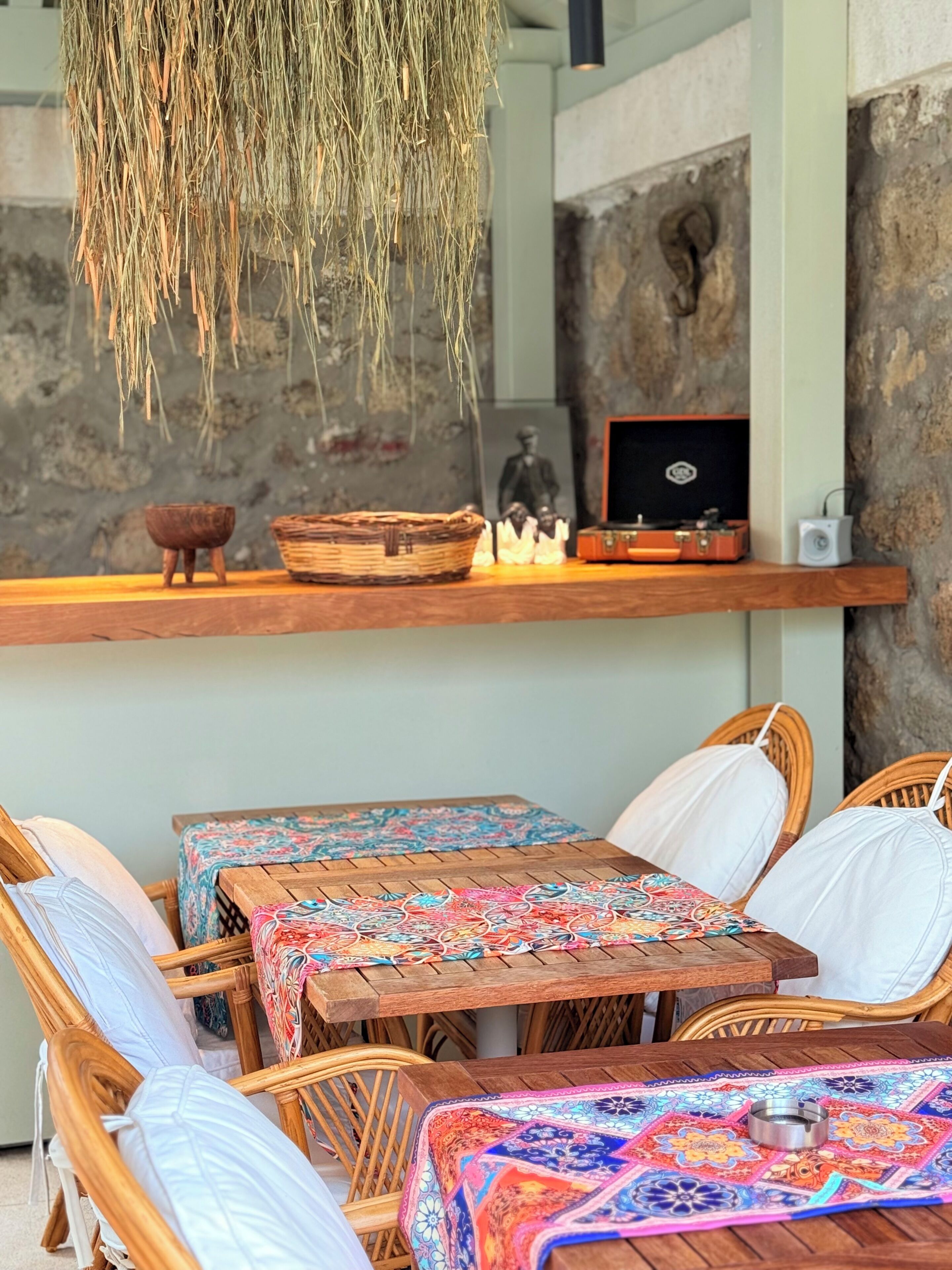A rustic outdoor seating area with wicker chairs and tables, a hanging plant, and a shelf with decorative items.