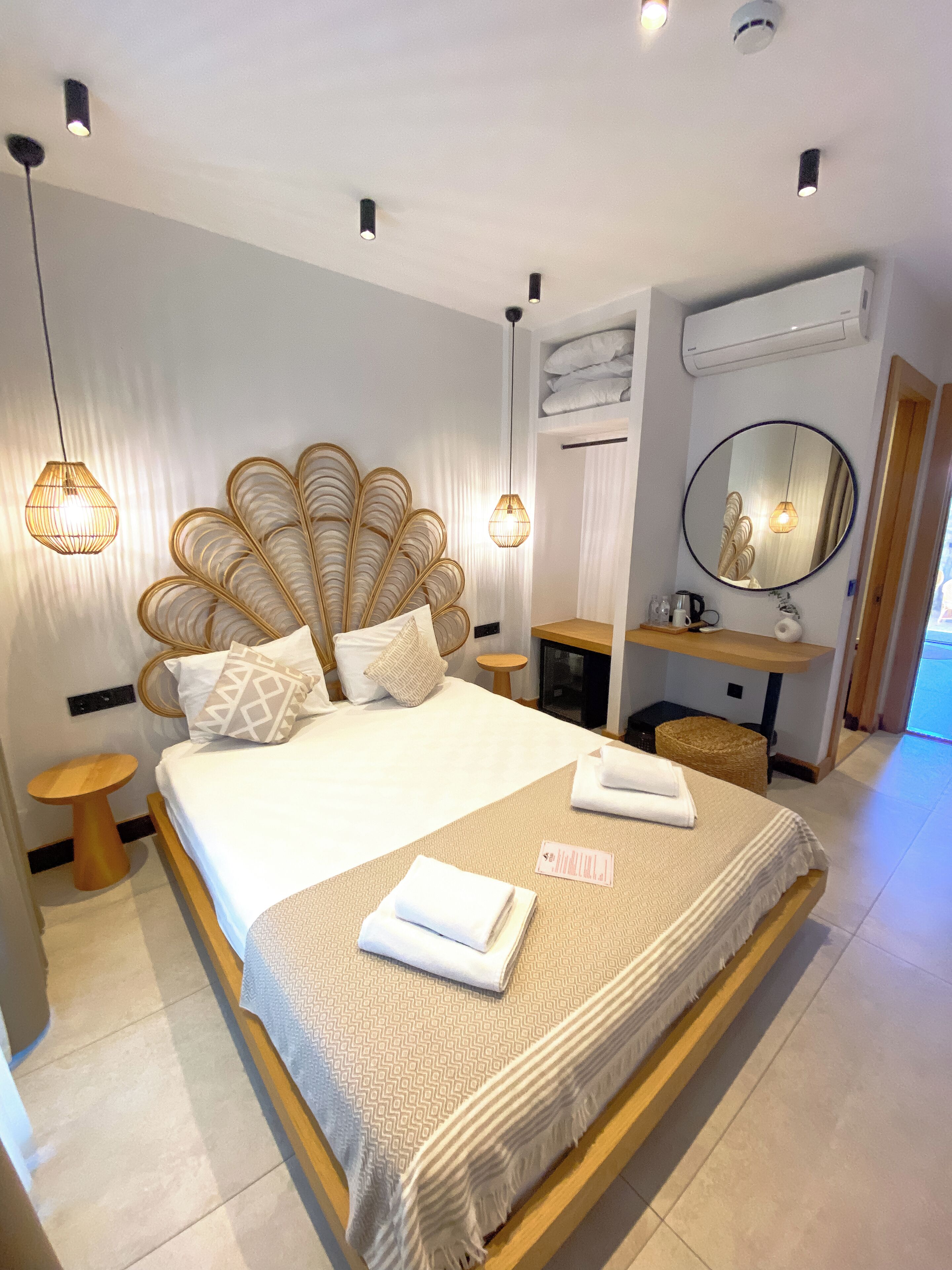 A modern hotel room with a large bed, bedside tables, a round mirror, and a built-in air conditioning unit.