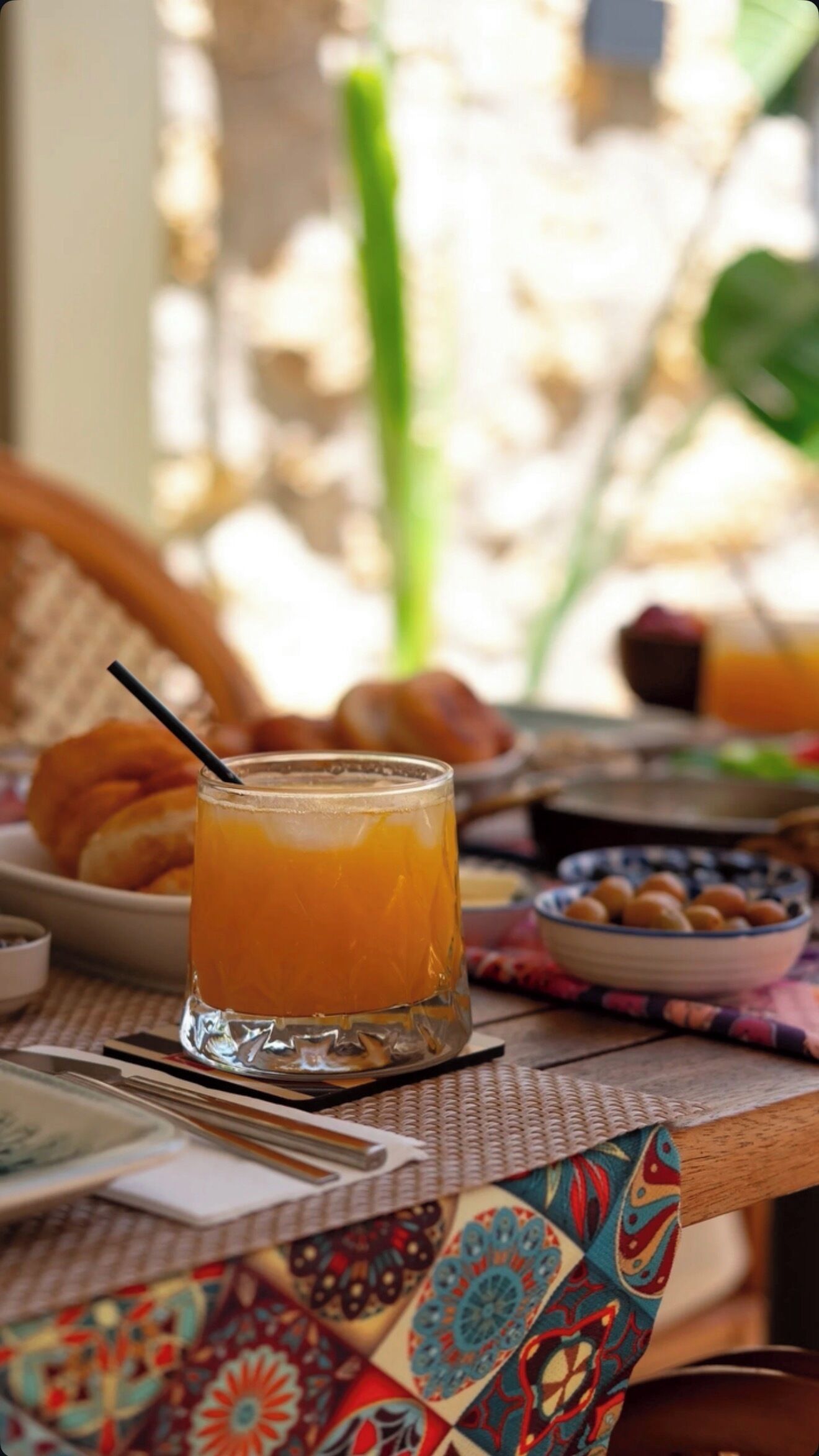 Une table avec un verre de jus d’orange, une assiette de croissants et un saladier de fruits.