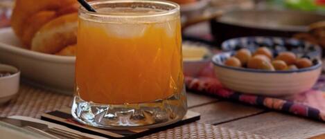 Une table avec un verre de jus d’orange, une assiette de croissants et un saladier de fruits.