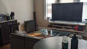 Un soggiorno con divano, tavolino in vetro, televisore e termosifone.