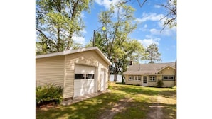 Une maison de plain-pied avec un garage, entourée d’arbres et d’une pelouse.
