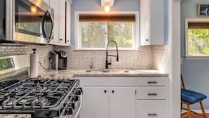 Une cuisine moderne avec des armoires blanches, une cuisinière en acier inoxydable et une fenêtre qui laisse entrer la lumière naturelle.