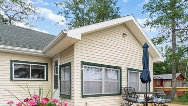 Une maison avec une terrasse en bois, une table de patio avec des chaises et un pot de fleurs orné de fleurs roses.