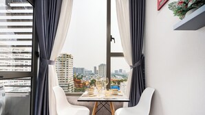 Ein Essbereich mit Tisch für zwei Personen, zwei weißen Stühlen und Blick auf die Stadt durch ein mit Vorhängen drapiertes Fenster.