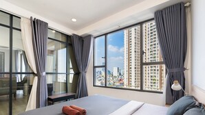 Ein modernes Hotelzimmer mit einem großen Bett, einem Schreibtisch und Blick auf die Stadt durch große Fenster.